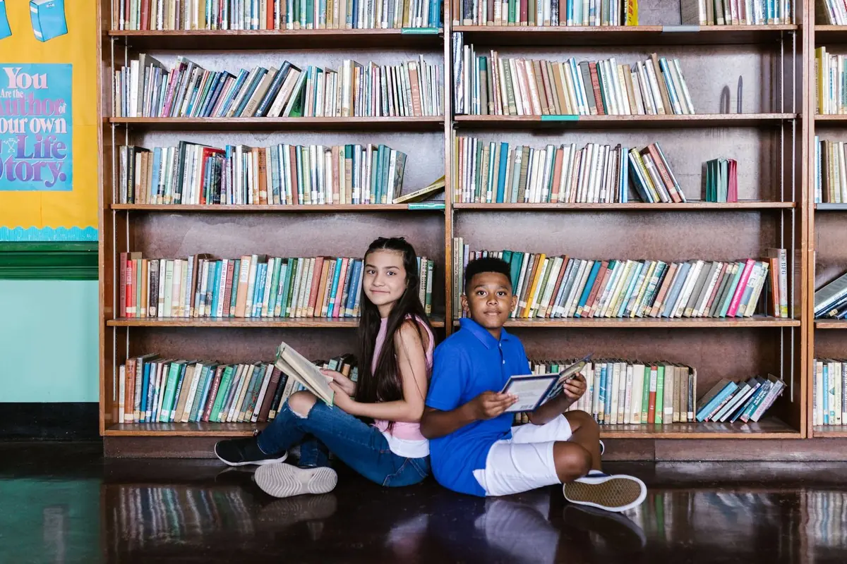 Estudiantes consultando libros en las mesas de la biblioteca escolar