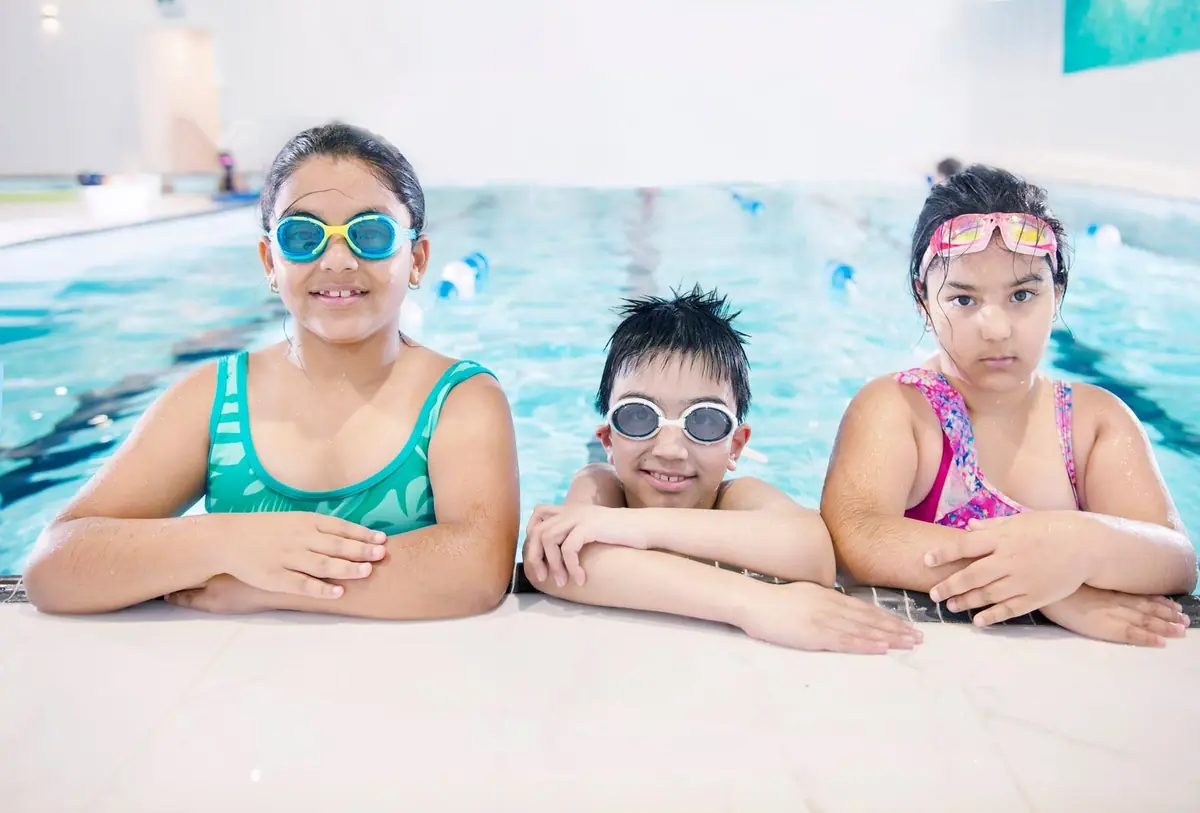 Niñas con gafas de natación descansando al borde de la piscina del colegio